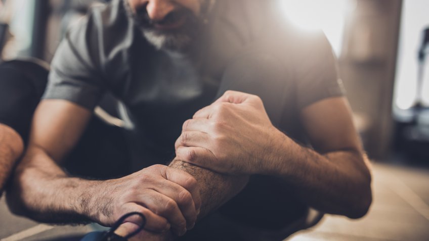 Close up of senior man holding his leg in pain while being on sports training in a health club.