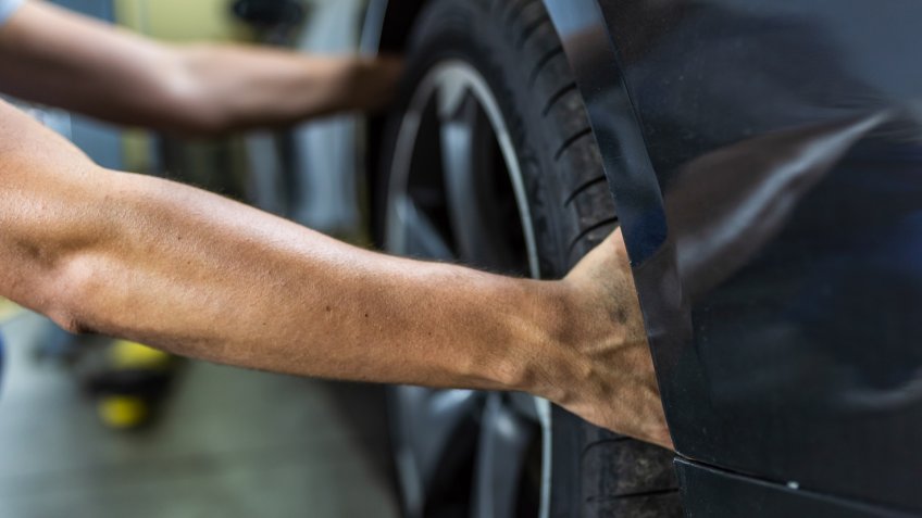 Photo of a young Unrecognizable auto mechanic in uniform is examining a tire while working in auto service.