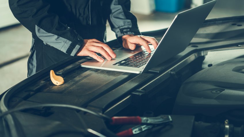 Car Mechanic with Laptop Computer Placed Near the Vehicle Engine.