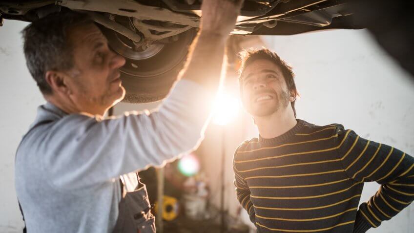 Senior mechanic working at car service,fixing broken car ,talking with client.