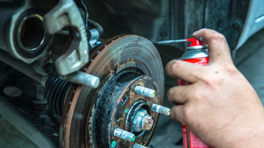 mechanic spraying lubricant on brake rotor