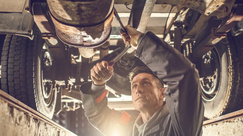 Mid adult auto mechanic working on a chassis in auto repair shop.