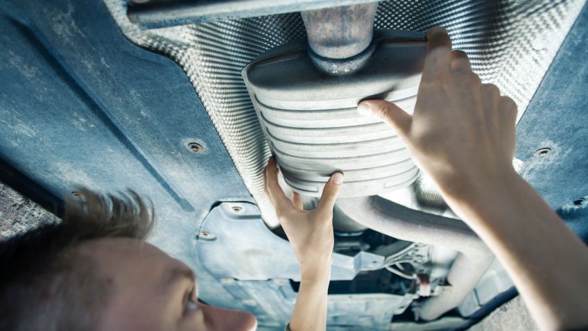 Male mechanic replacing exhaust pipe under car.