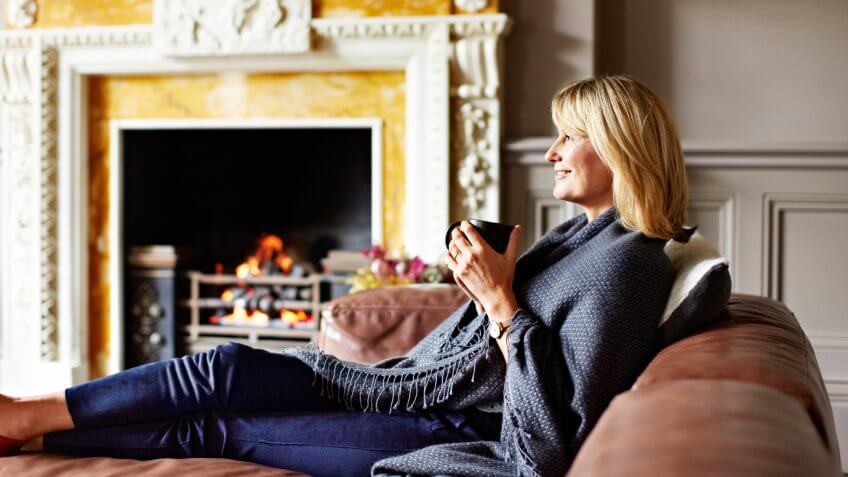 Shot of a mature woman sitting on her sofa drinking tea while wrapped in a blanket.