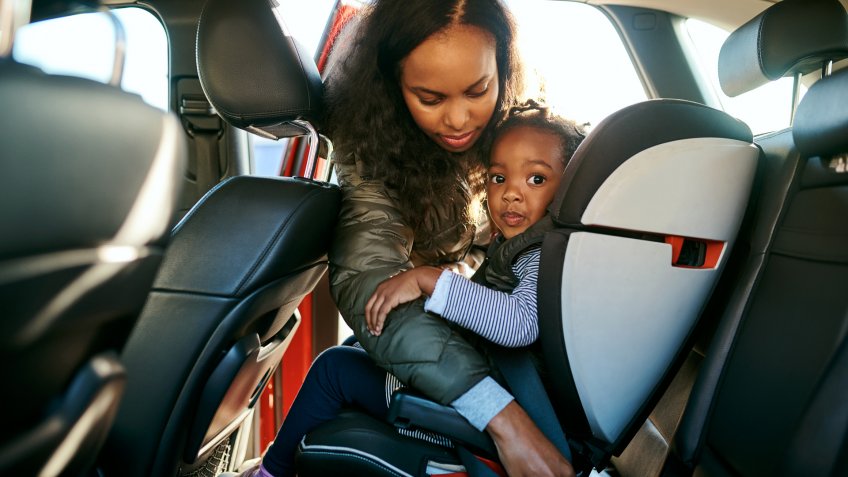 Shot of an adorable little girl being secured in her car seat by her mother.