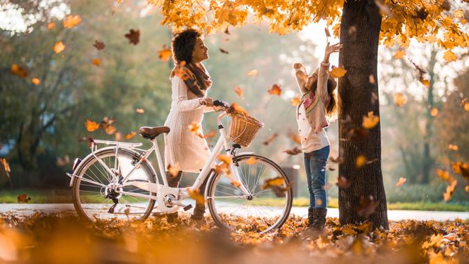 Happy African American mother with a bike enjoying with her daughter in autumn day.