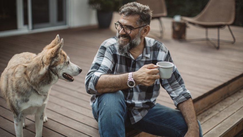 Mature men at his cottage resting on porch with his dog.
