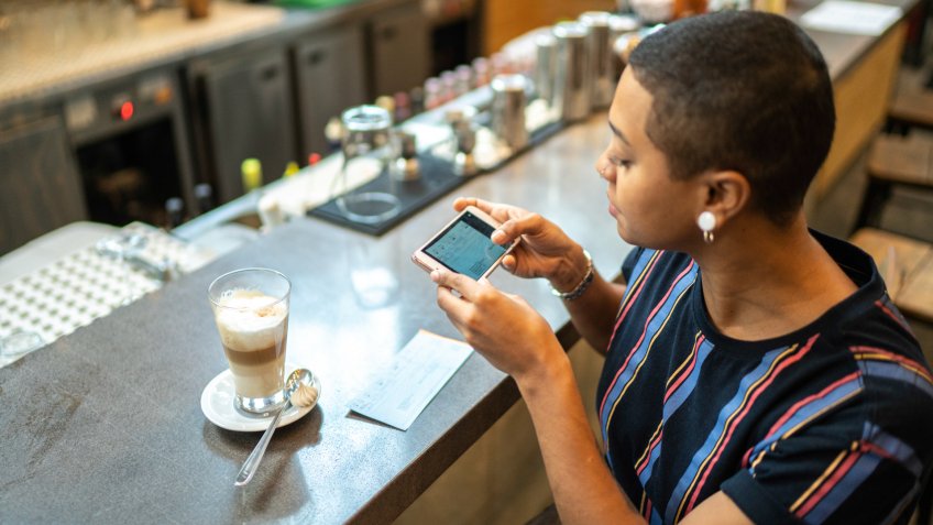 Young woman depositing check by phone in the cafe.