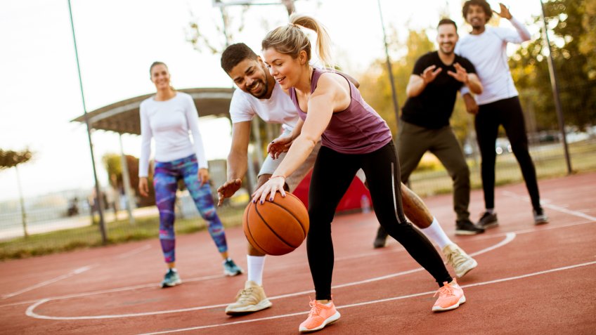Group of multiracial young people playing basketball on court at outdoors.