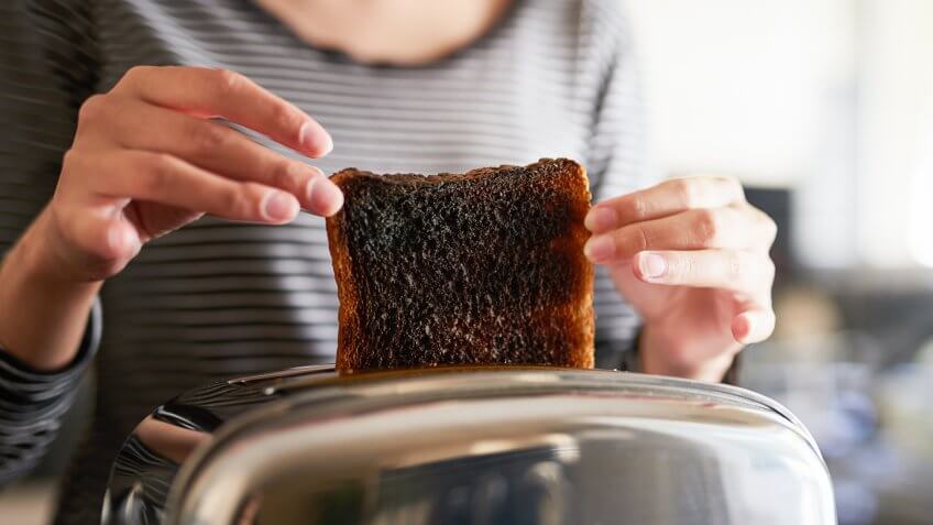Cropped shot of a woman removing a slice of burnt toast from a toaster at home.