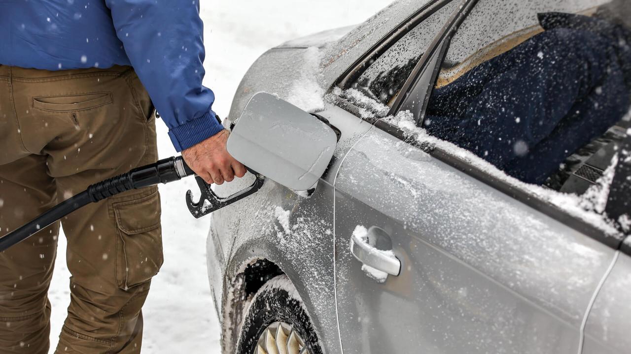 Man holding fuel nozzle, filling gas tank of car covered with snow in winter.