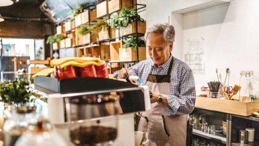 Professional senior barista working in a cafe, preparing coffee.