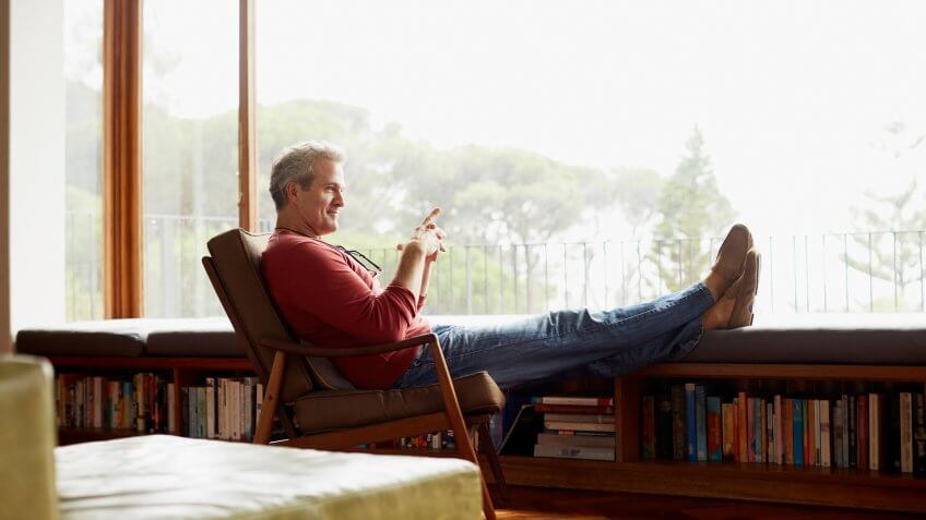 Full length side view of thoughtful mature man relaxing on armchair at home.