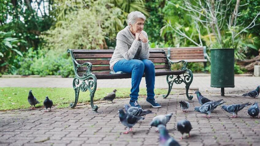 Shot of a senior woman sitting on a park bench and looking thoughtful.