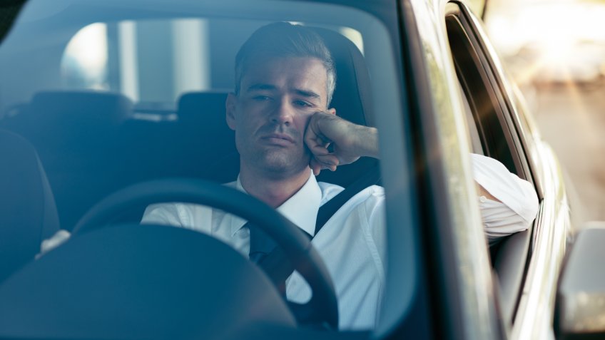 Pensive disappointed businessman sitting in his car and thinking with hand on chin.