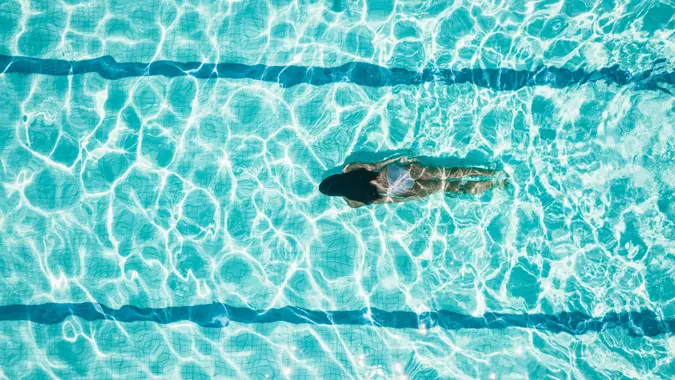 Drone view on teenage girl diving in blue swimming pool.