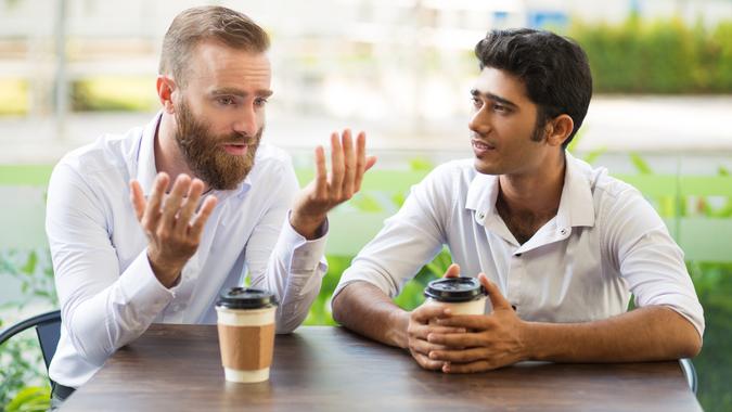 Two male friends drinking coffee and talking in outdoor cafe.