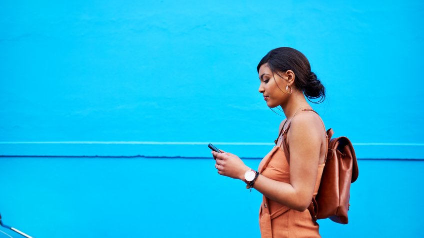 Shot of an attractive young woman using a cellphone while traveling with her bicycle against a blue background outdoors.