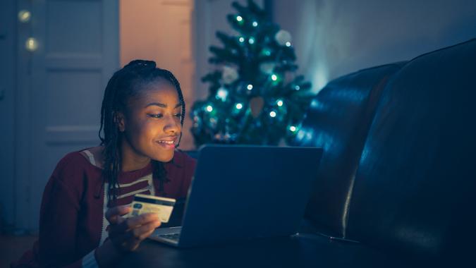 Beautiful young African women shopping Christmas presents online at home, using credit card.