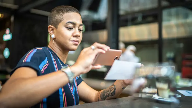 Young woman depositing check by phone in the cafe.