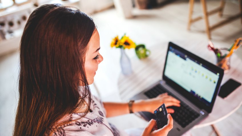 Pregnant woman with credit card and laptop buying goods online at home.