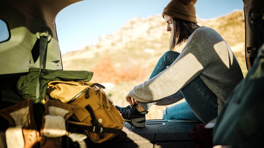 Young woman sitting in car trunk and tying her shoelaces on snickers.