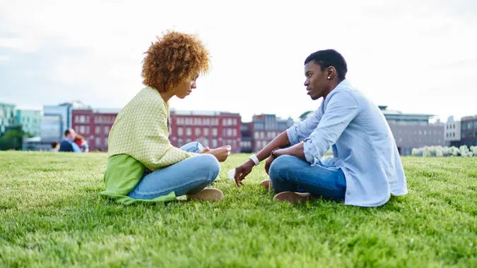 Two african american friends dressed in casual wear sitting against each other and communicating having conflict in relationship.