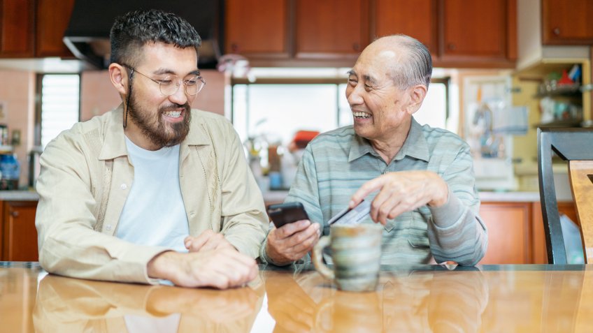 A young man is helping his grand father with shopping online and using a credit card on a smart phone.