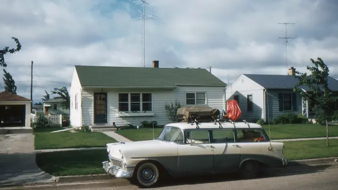 1956 Chevrolet station wagon packed for vacation in front of new tract house with TV antenna.