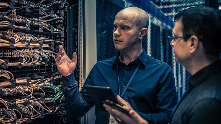 Photo of an IT engineer with a digital tablet explaining server configuration and operation to his supervisor.