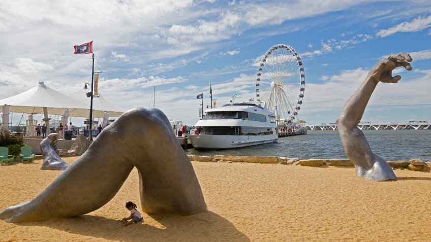 OXON HILL, MARYLAND, USA - SEPTEMBER 11, 2016: A sculpture Awakening at waterfront of National Harbor with a child playing in its shadow.