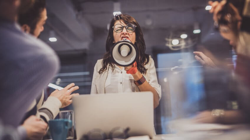 Low angle view of angry female manager yelling at her team through megaphone in the office.