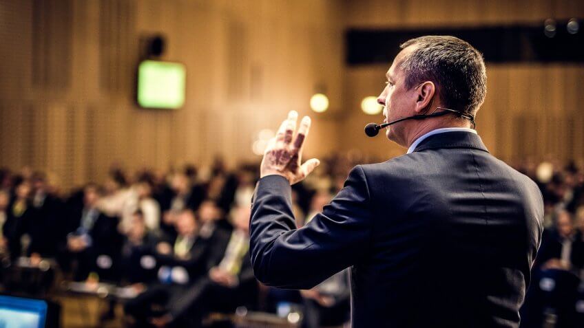 Rear view of a businessman entrepreneur giving a lecture to a sold-out crowd in a lecture hall.
