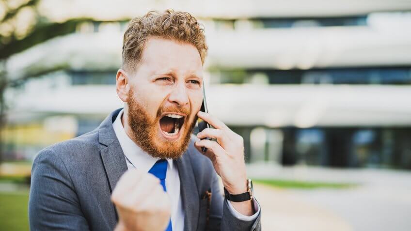 Crazy young businessman shouting loud while on the phone.