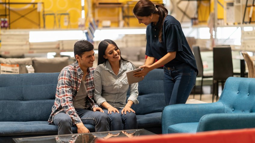 Happy saleswoman selling furniture to a couple at a home improvement store and showing them options on a tablet computer.