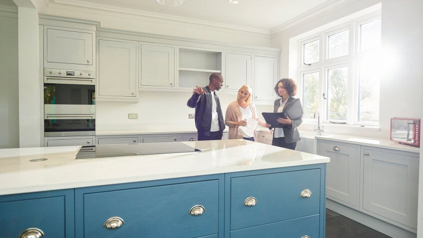a saleswoman or estate agent shows a couple around a home with new kitchen.