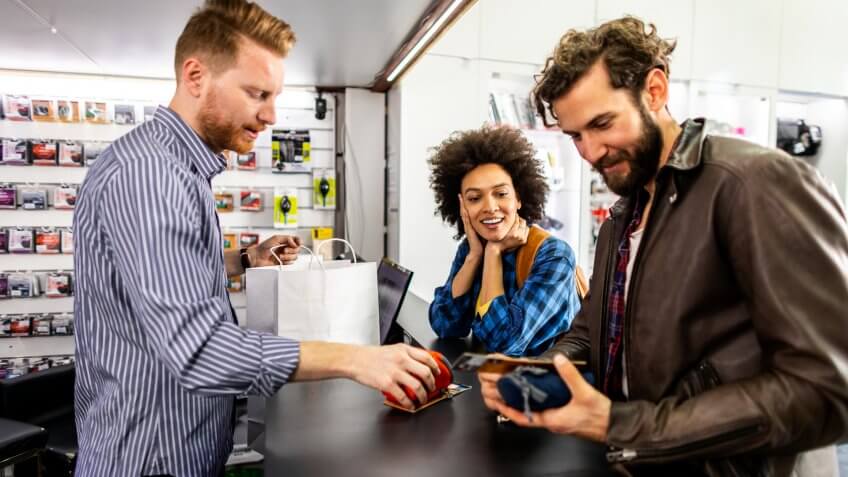 Store clerk getting a small camera pouch ready by putting it in a white paper shopping bag for the happy customer couple in a camera store.