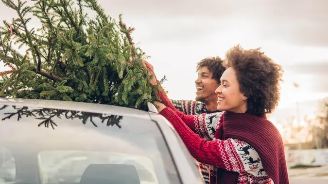 Happy young couple strapping Christmas tree to their car.