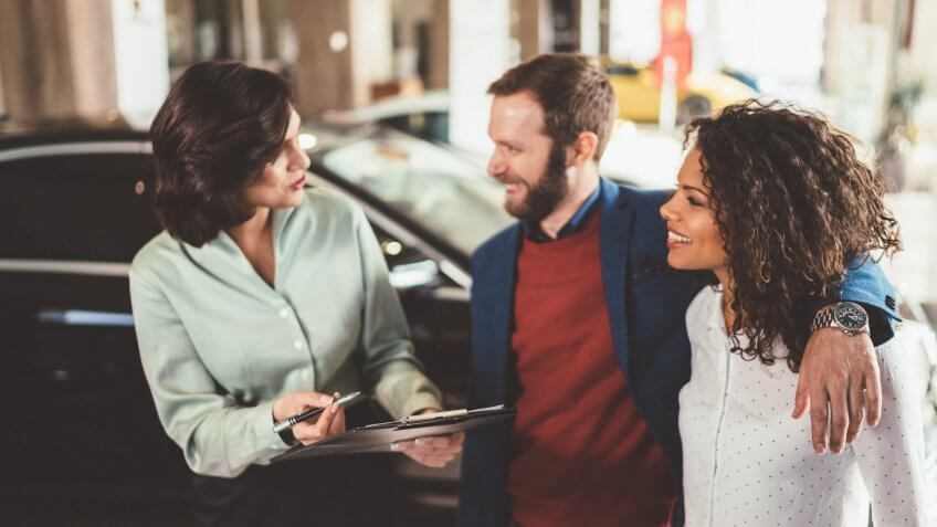 Car saleswoman assisting customers to make the best choice for buying a new car in the showroom.