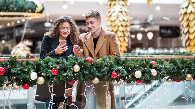 A happy young couple with smartphone in shopping center at Christmas time, text messaging.