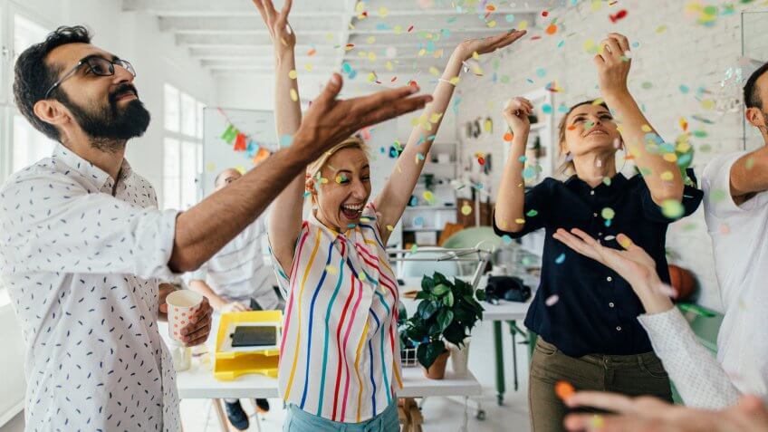 Photo of a group of coworkers having a happy occasion and celebrating together in their office.