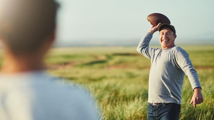 Shot of father throwing a football to his son on a field.