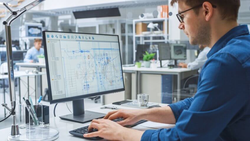 Over the Shoulder Shot of Engineer Working with CAD Software on Desktop Computer, Screen Shows Technical Drafts and Drawings.