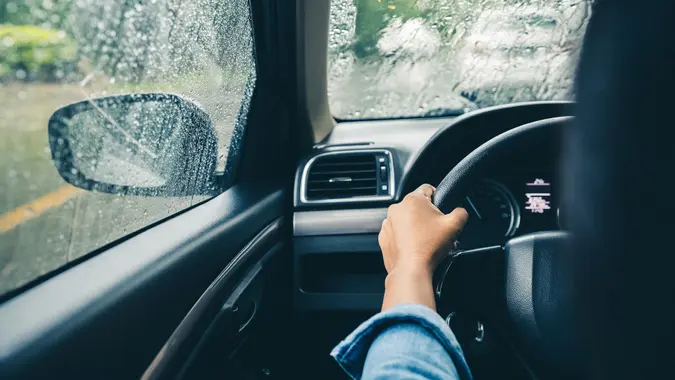 closeup driver's hands on steering wheel driving on rainy day.