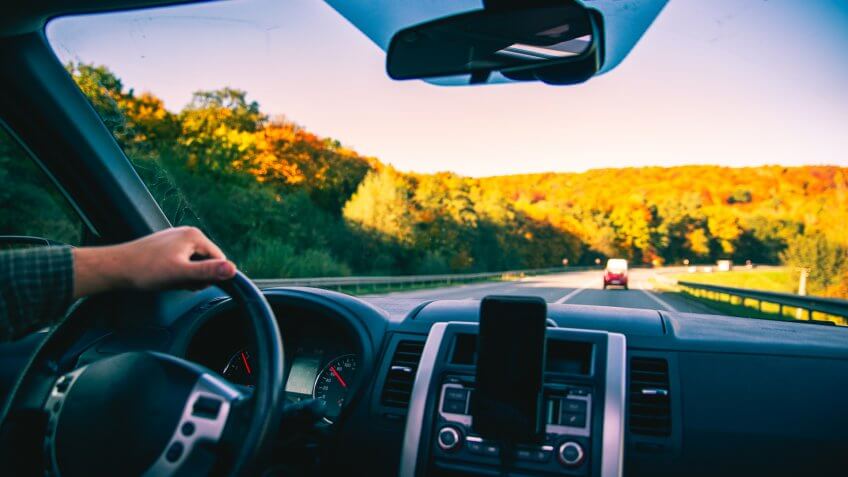man hands on steering wheel riding by autumn speedway fall season car travel.