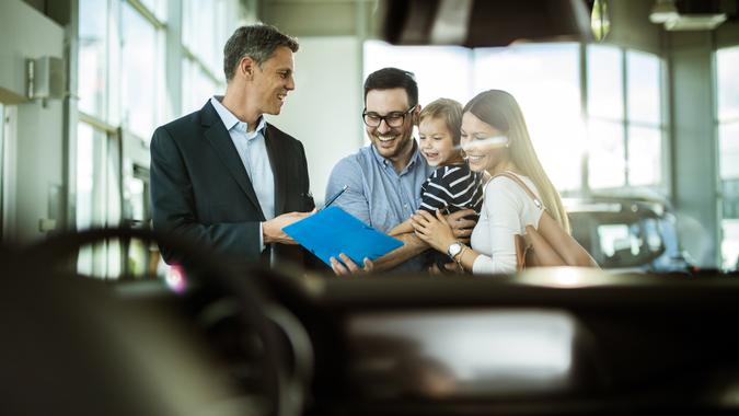 Happy family reading buying plan with salesperson in a car showroom.