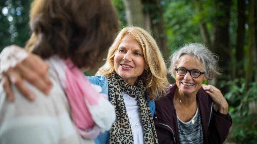 Mature woman sitting arms around friends at lakeshore.
