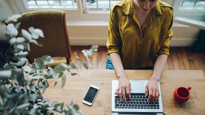 Vintage toned portrait of a young female novelist, blogger or a freelancer designer working on the laptop while having a cup of coffee in her living room in the beautiful bright apartment in Paris city center, in Montmartre district.