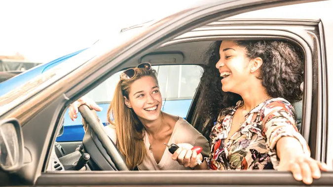 Young female best friends having fun at car roadtrip moment - Transportation concept and urban ordinary life with women girlfriends at happy travel vacation on the road - Bright azure filter.
