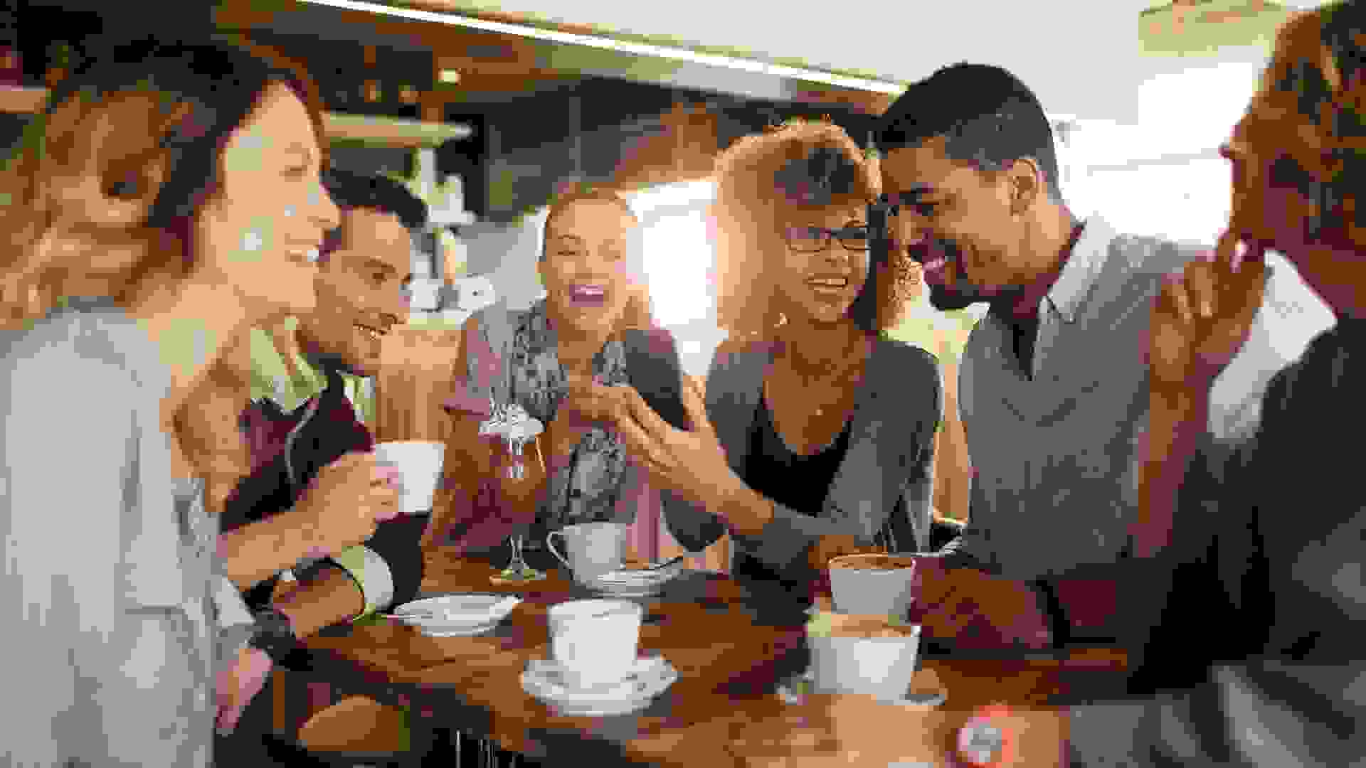 Picture of friends smiling and sitting in a cafe having coffee and using a phone.